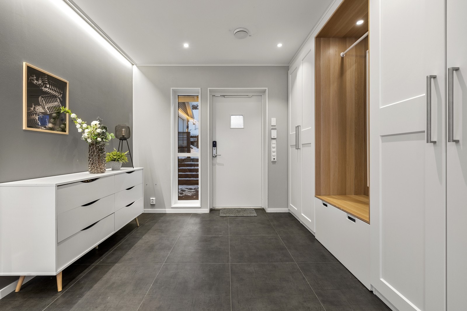 Innbydende entré med flislagt gulv, tidsriktig innredning og plass til yttertøy og sko. Downlights i taket. Galleribilde