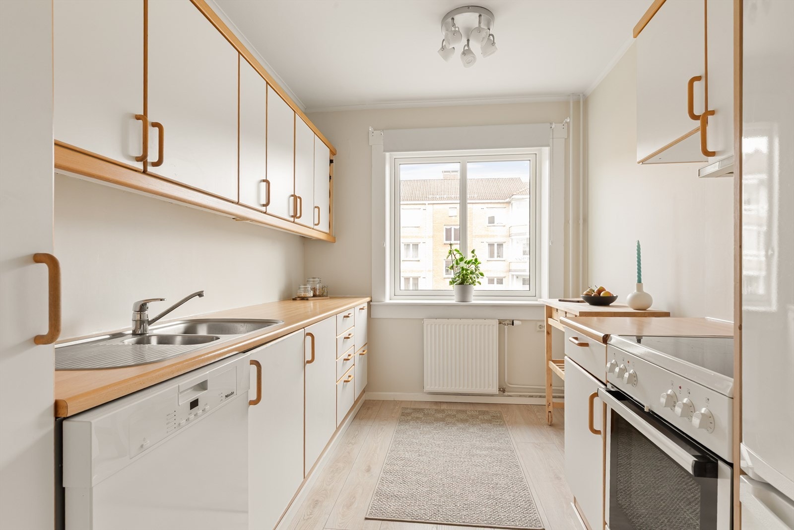 Kjøkkeninnredning med hvite, glatte fronter. Laminat benkeplate med nedfelt kum i rustfritt stål. Galleribilde