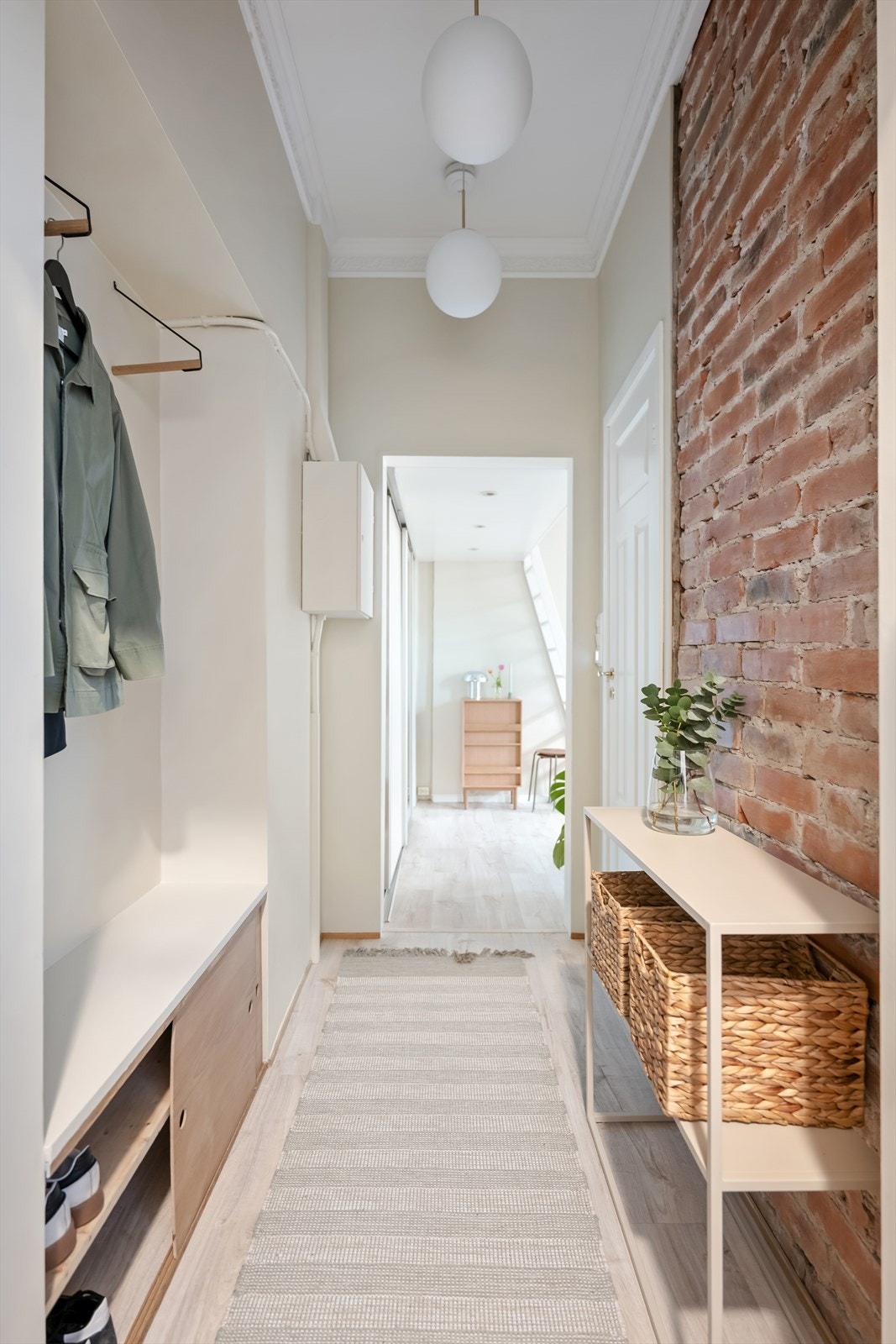 Entréen er lys og innbydende med eksponert teglsteinsvegg og god takhøyde. Veggene i leiligheten ble malt i 2024. Galleribilde
