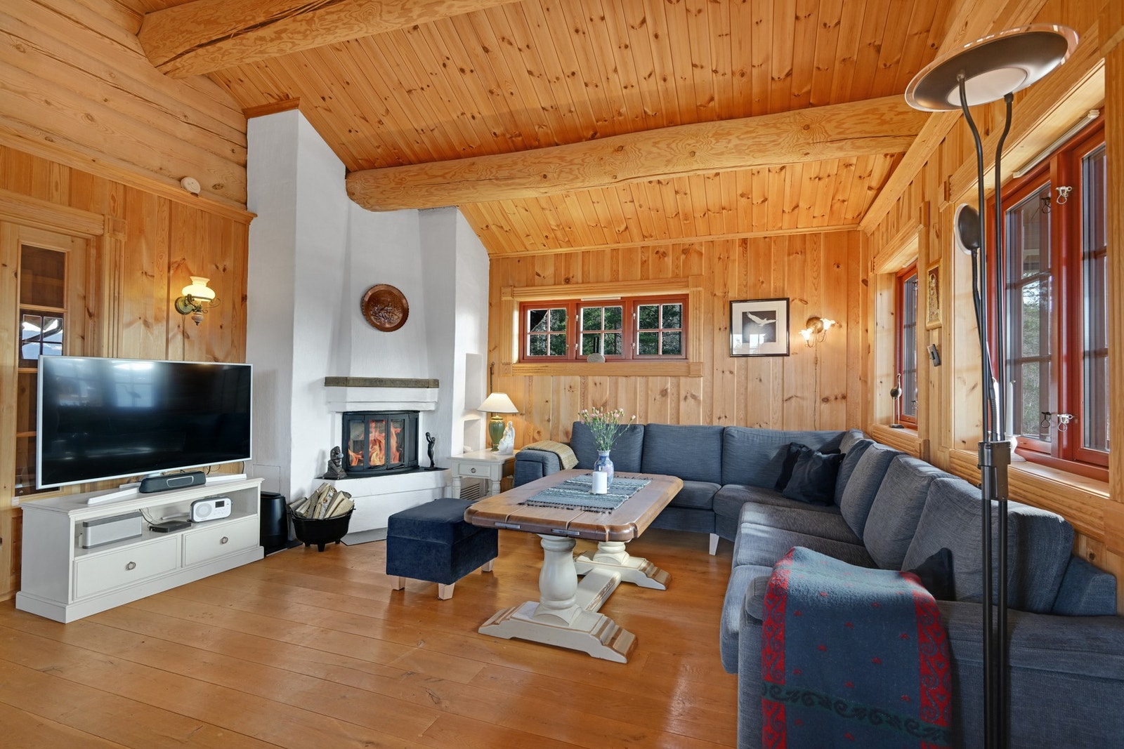 Lun og innbydende stue med gjennomgående trepanel, synlige bjelker og peis som skaper en varm hyttefølelse. Galleribilde