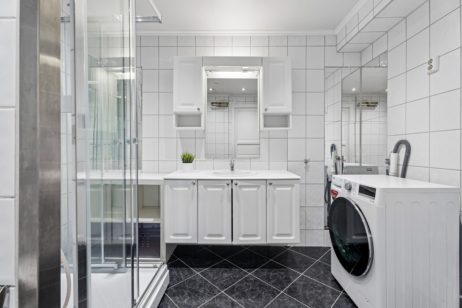 Helfliset bad på 6,7 m² med dusjkabinett, opplegg for vaskemaskin og servant med god oppbevaringsplass. Galleribilde