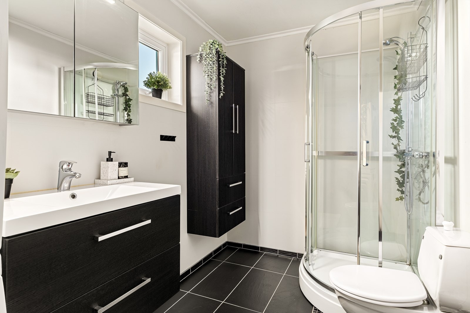 Pent og praktisk bad/vaskerom med fliselagt gulv som gir et rent og moderne uttrykk. Rommet er utstyrt med dusjkabinett og toalett, og har god plass til vaskemaskin og oppbevaring - en funksjonell løsning for en komfortabel hverdag. Galleribilde