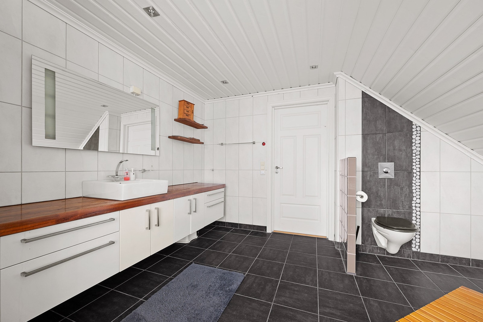 Badet er utstyrt med vegghengt toalett, en bred servantinnredning og en dusjnisje med vegg av glassbyggestein. Galleribilde