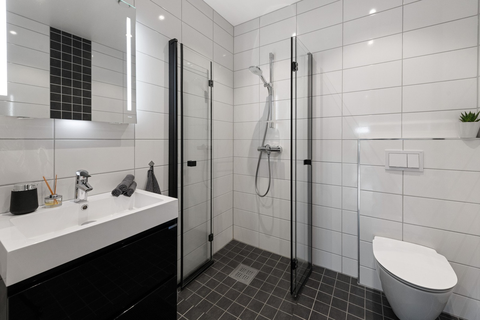 Baderomsinnredning med heldekkende servant og underskap med skuffer, veggmontert toalett og dusjhjørne med innfellbare dører i herdet glass. Badet har gulvvarme Galleribilde