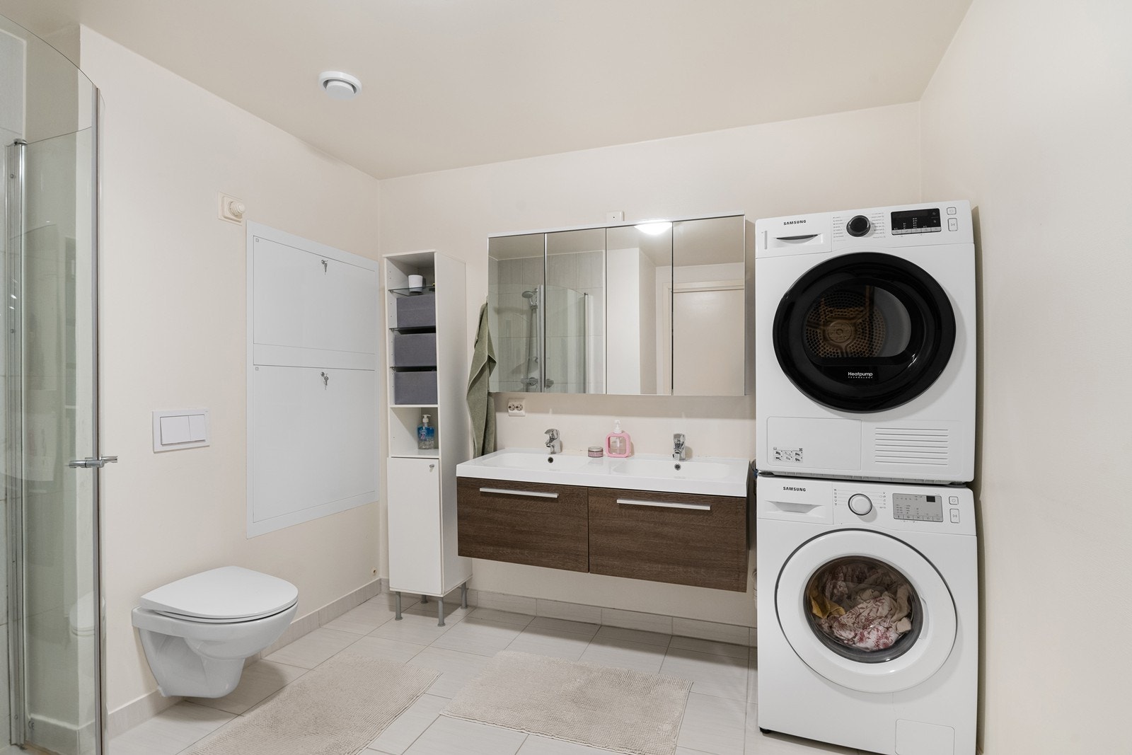 Badet har moderne innredning med to nedfelte servanter, veggmontert toalett og dusjhjørne med glassvegger. Det er også opplegg for vaskemaskin, noe som gjør rommet både funksjonelt og praktisk. Galleribilde