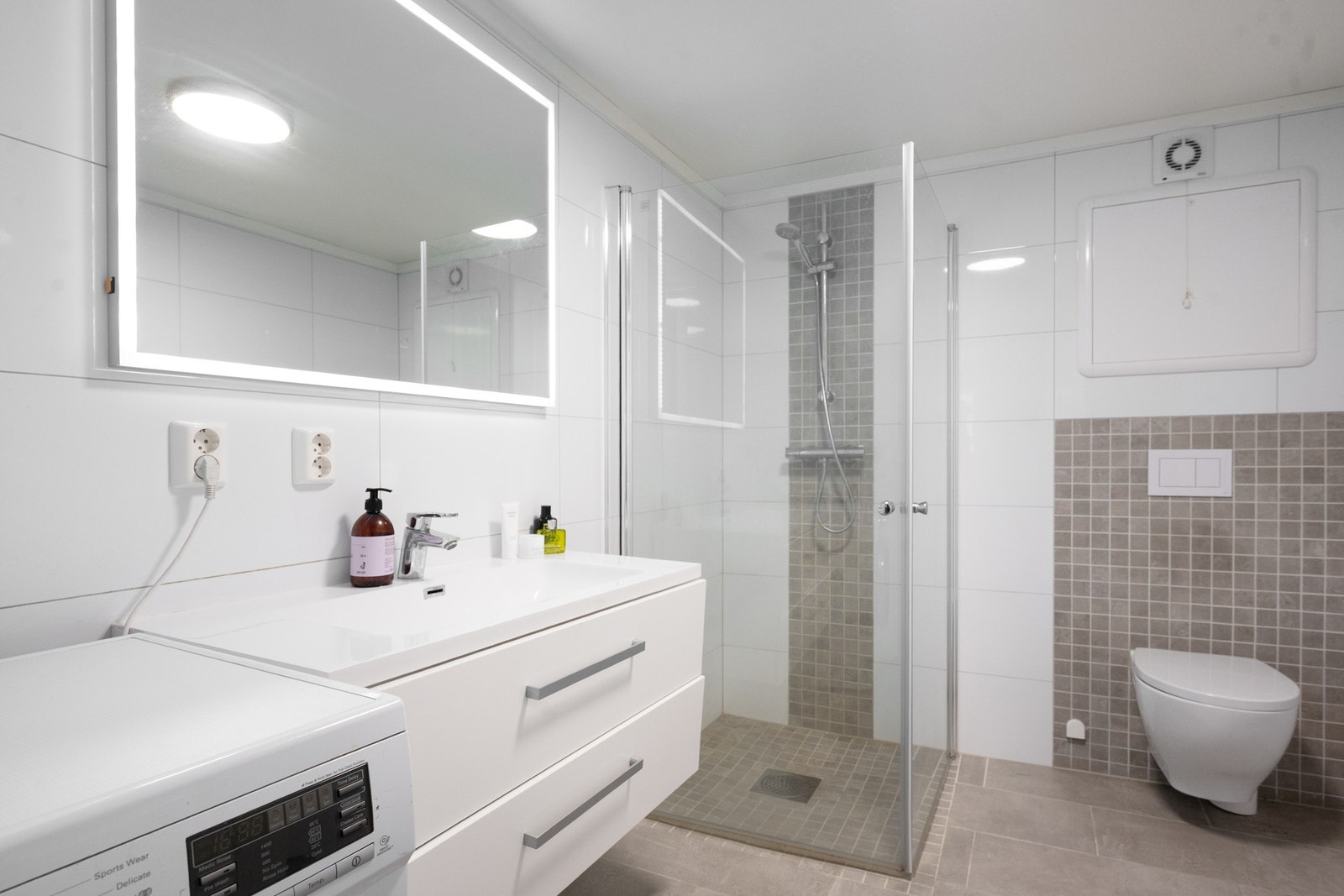 Bad med dusjhjørne, vegghengt toalett og servant med oppbevaringsskuffer. Galleribilde