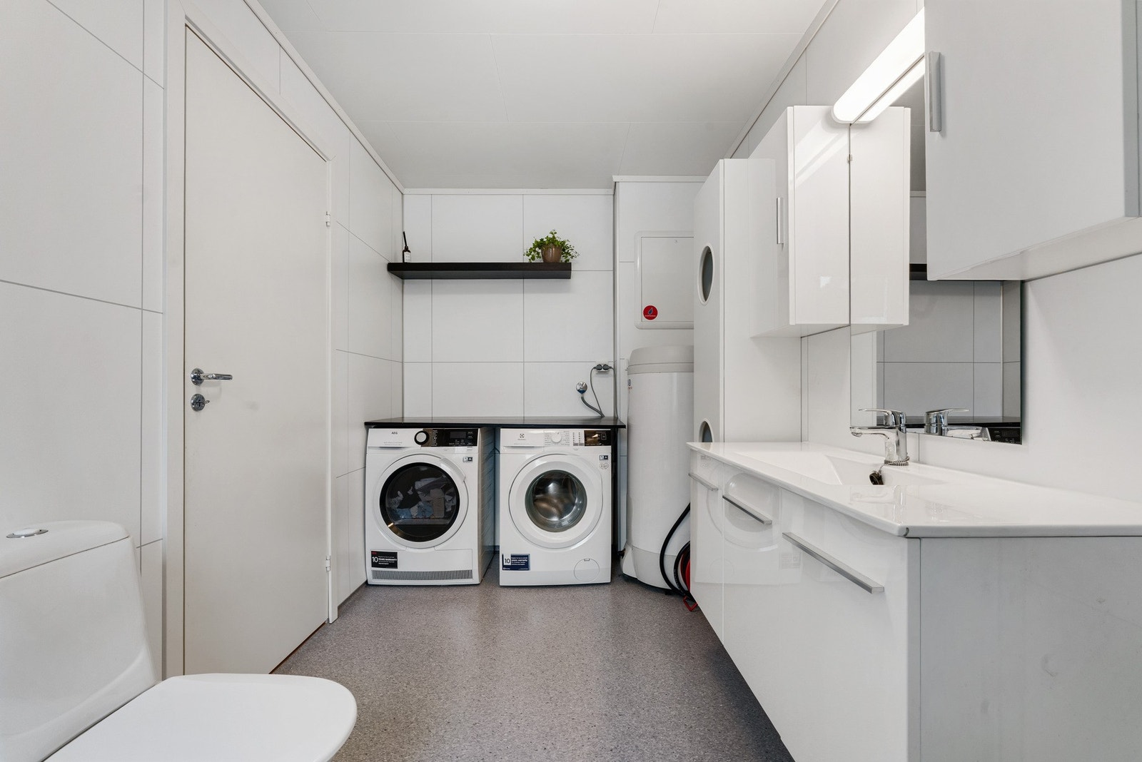 Her er det praktisk vaskeromsinnredning med brettebenk, hylle over brettebenk og opplegg for vaskemaskin og tørketrommel Galleribilde