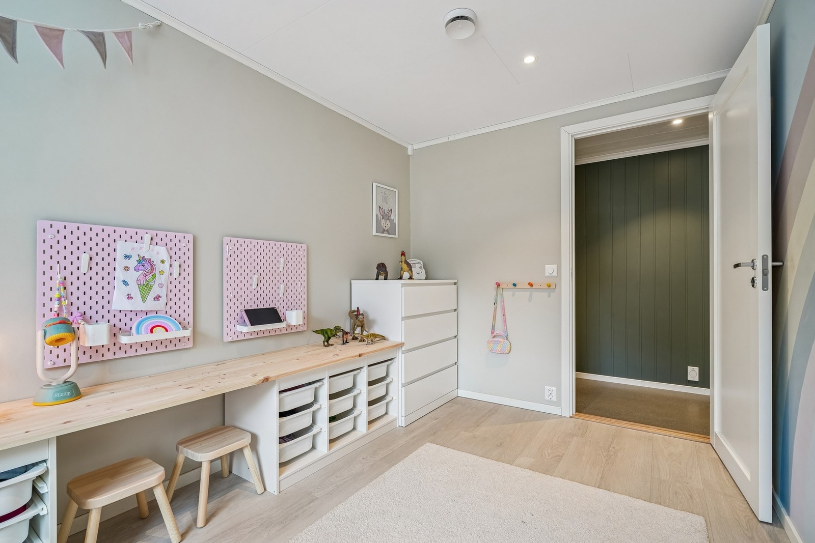 Barnerommet har lys veggdekor, stort vindu og praktisk oppbevaringsløsning. Galleribilde