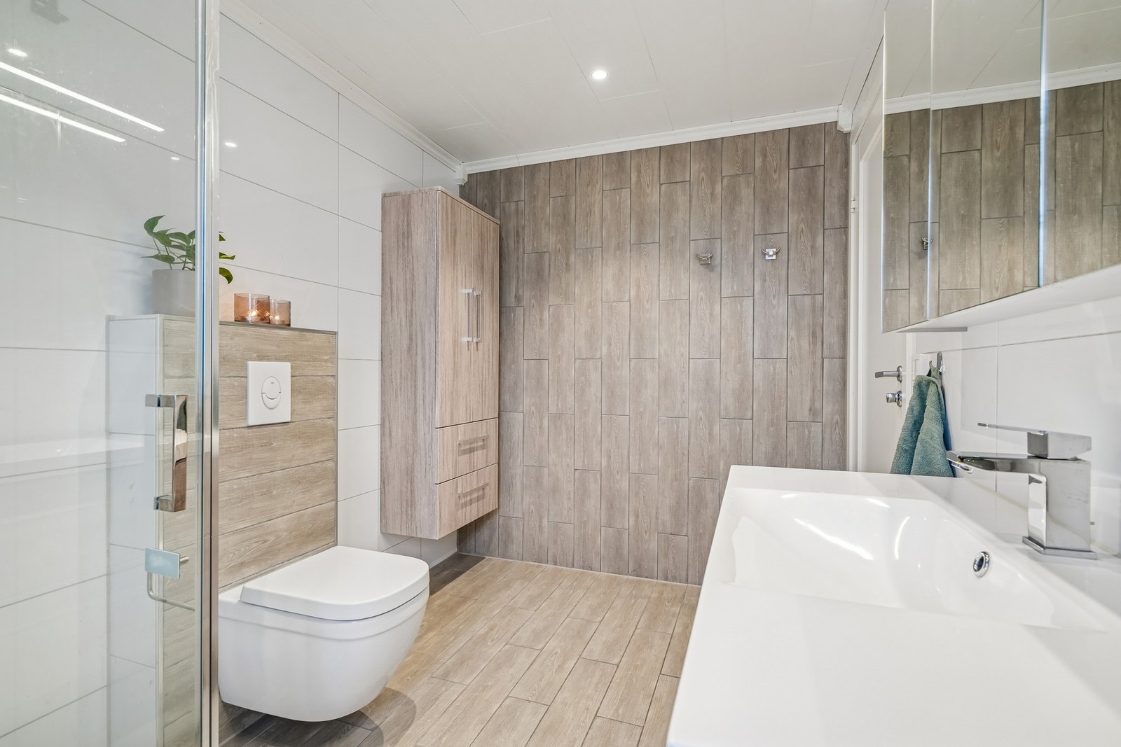 Badet er utstyrt med vegghengt toalett og dusjhjørne med glassdører. Galleribilde