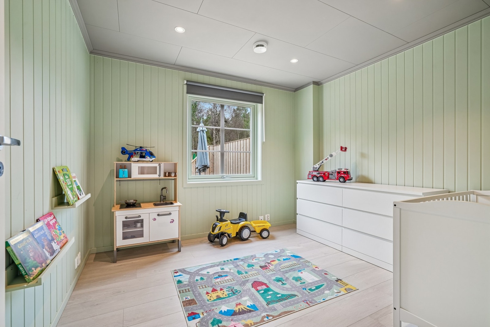 Barnerommet har panelvegger malt i en nydelig grønnfarge og et vindu som gir godt med naturlig lys. Galleribilde