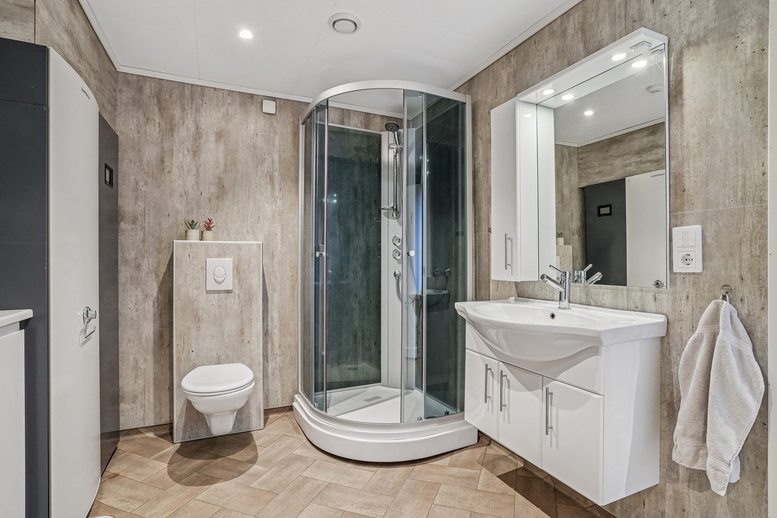 Bad/vaskerom er utstyrt med dusjkabinett, vegghengt toalett og baderomsinnredning med skapfronter og helstøpt servant. Speil med skap og belysning over. Galleribilde