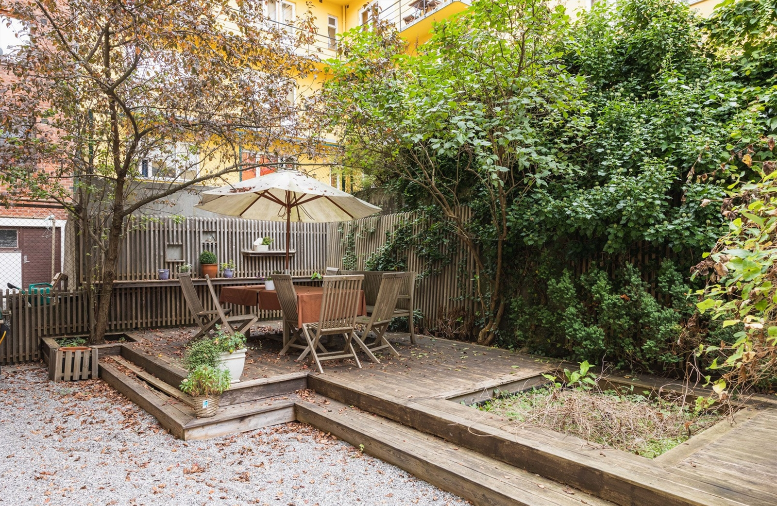 Avskjermet bakgård med beplantning, grusede arealer og terrasseplatting i trykkimpregnert virke. Galleribilde