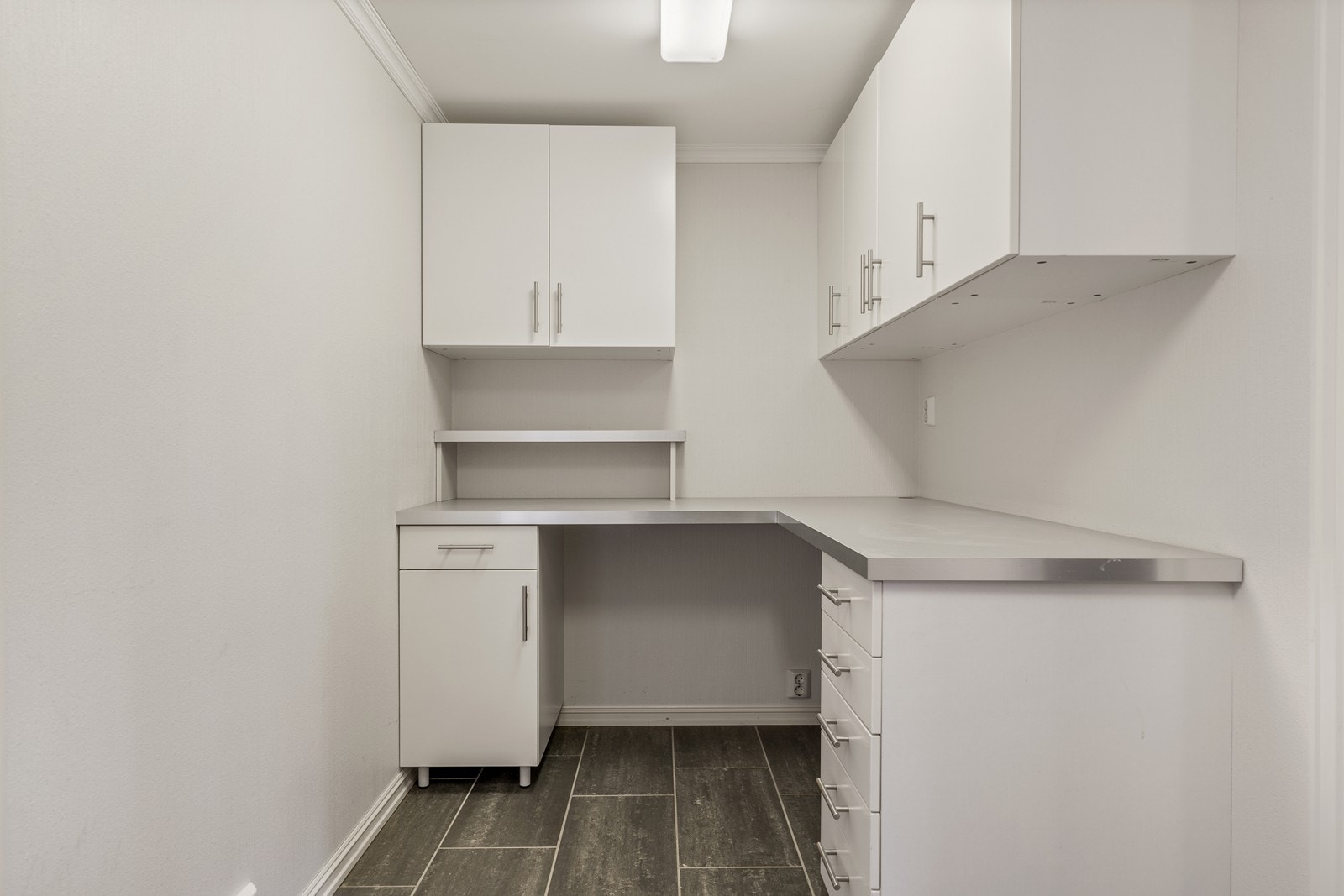 Kjekk bod med fliser på gulv, hjørneseksjon med benkeplate, overskap, underskuffer, ekstra benkeplate med dobbelt underskap i den andre enden av rommet inkl. dobbelt overskap og dobbelt garderobeskap. Galleribilde