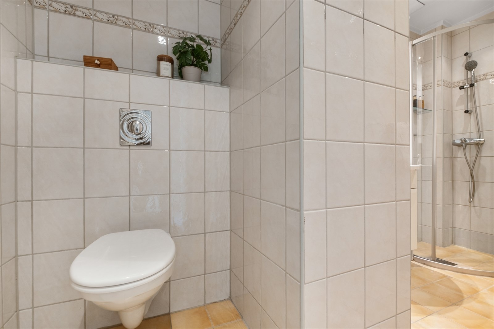 Rommet er utstyrt med dusjhjørne med skyvedører, veggmontert toalett samt servantskap med hvit servant og tilhørende blandebatteri Galleribilde