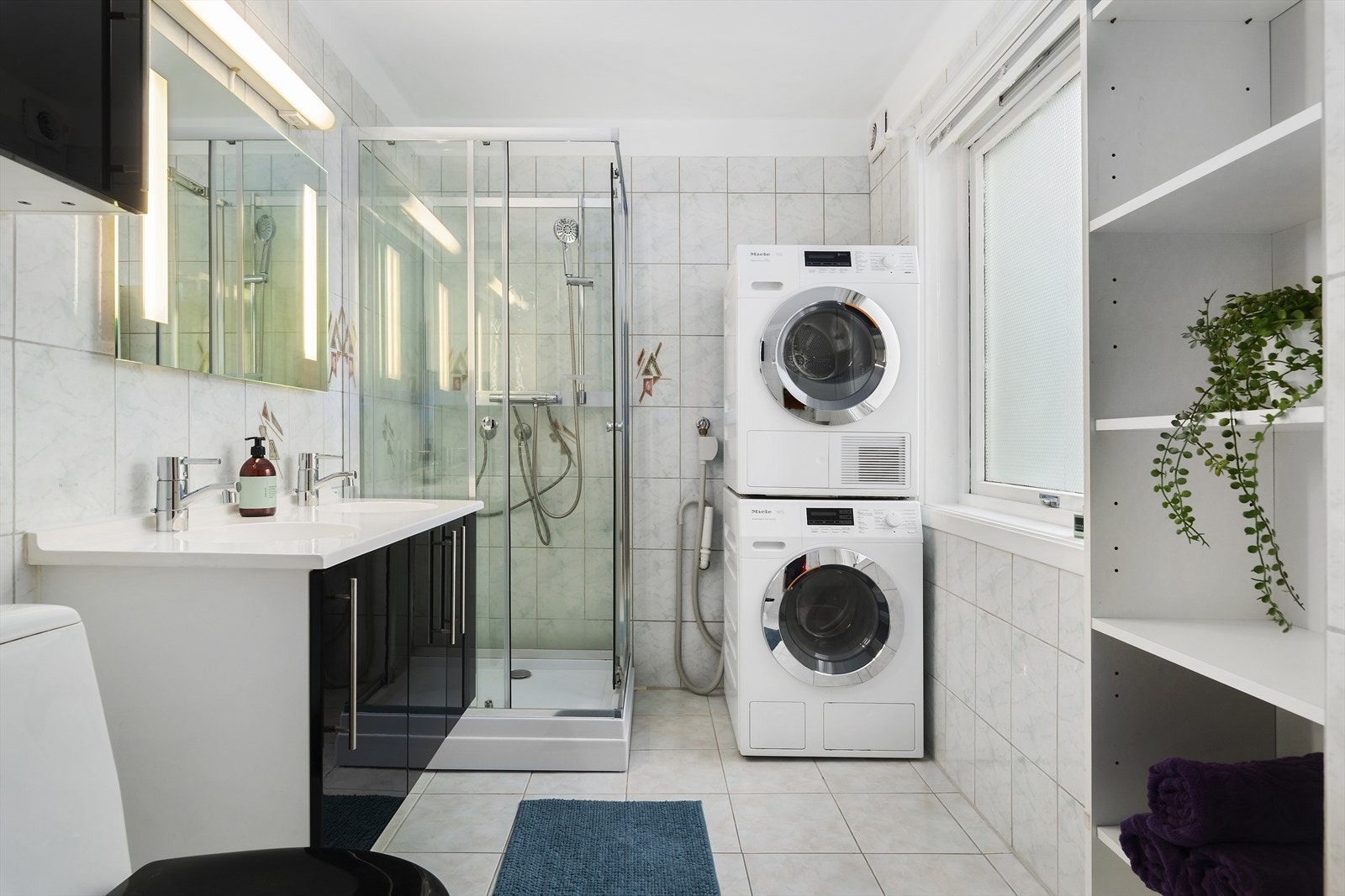 Badet har fliser på gulv og vegger. Her er dusjkabinett, toalett, innredning med servant og opplegg for vaskemaskin og tørketrommel. Galleribilde