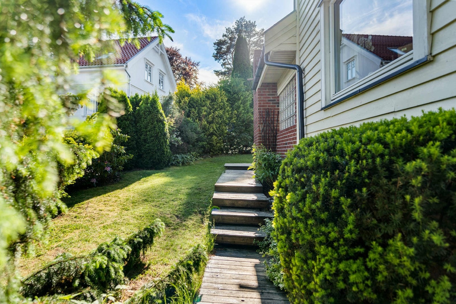 Vi tar turen til bakhagen, en skjermet og solrik uteplass med stor plen, frodig beplantning og plass til både lek og avslapning. Galleribilde
