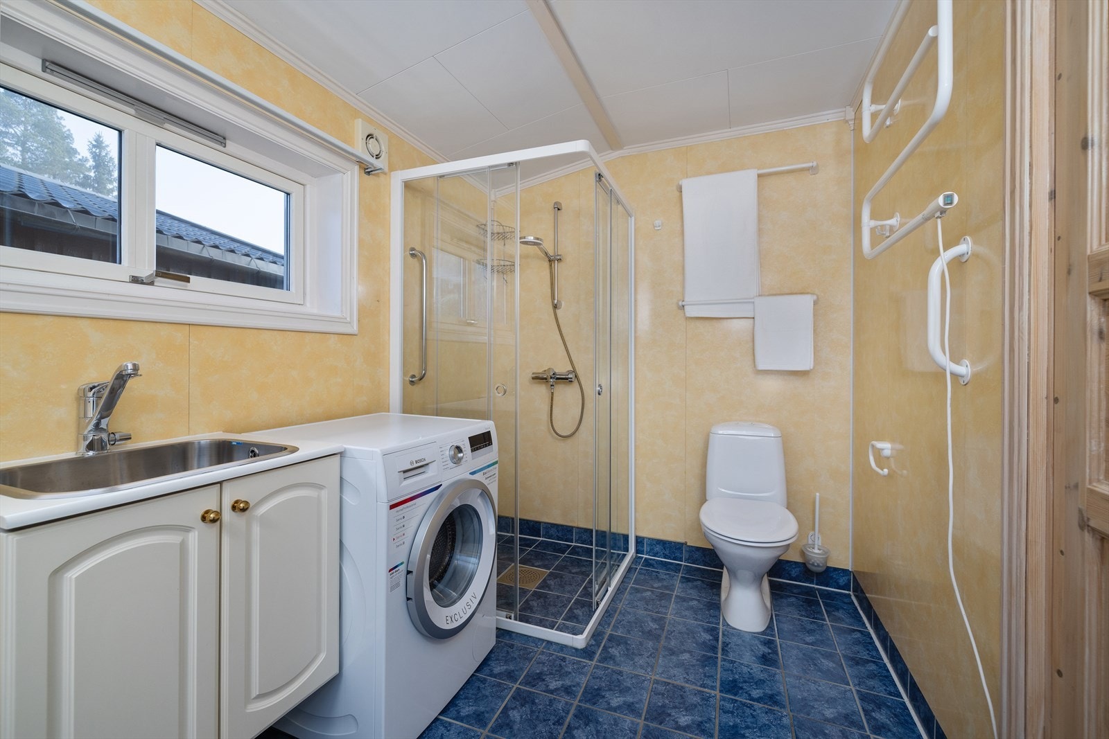 Badet er kombinert vaskerom med flislagt gulv, varmekabler og opplegg for vaskemaskin. Galleribilde
