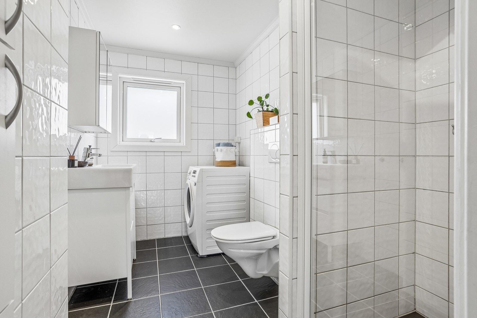 Flislagt bad med varmekabler i gulvet, vegghengt toalett og opplegg for vaskemaskin. Galleribilde