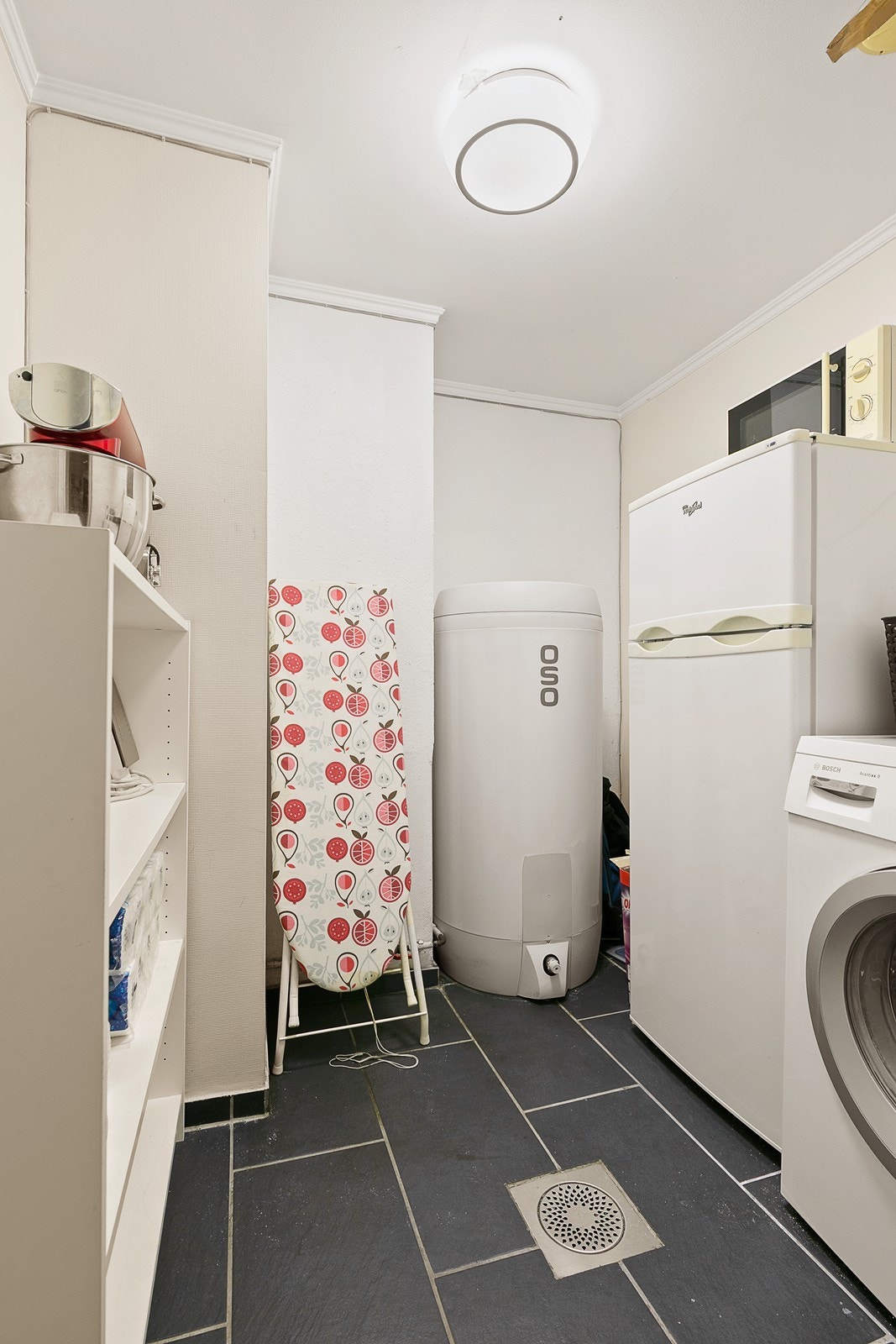 Praktisk vaskerom med opplegg for vaskemaskin, varmtvannsbereder og plass til lagring. Galleribilde