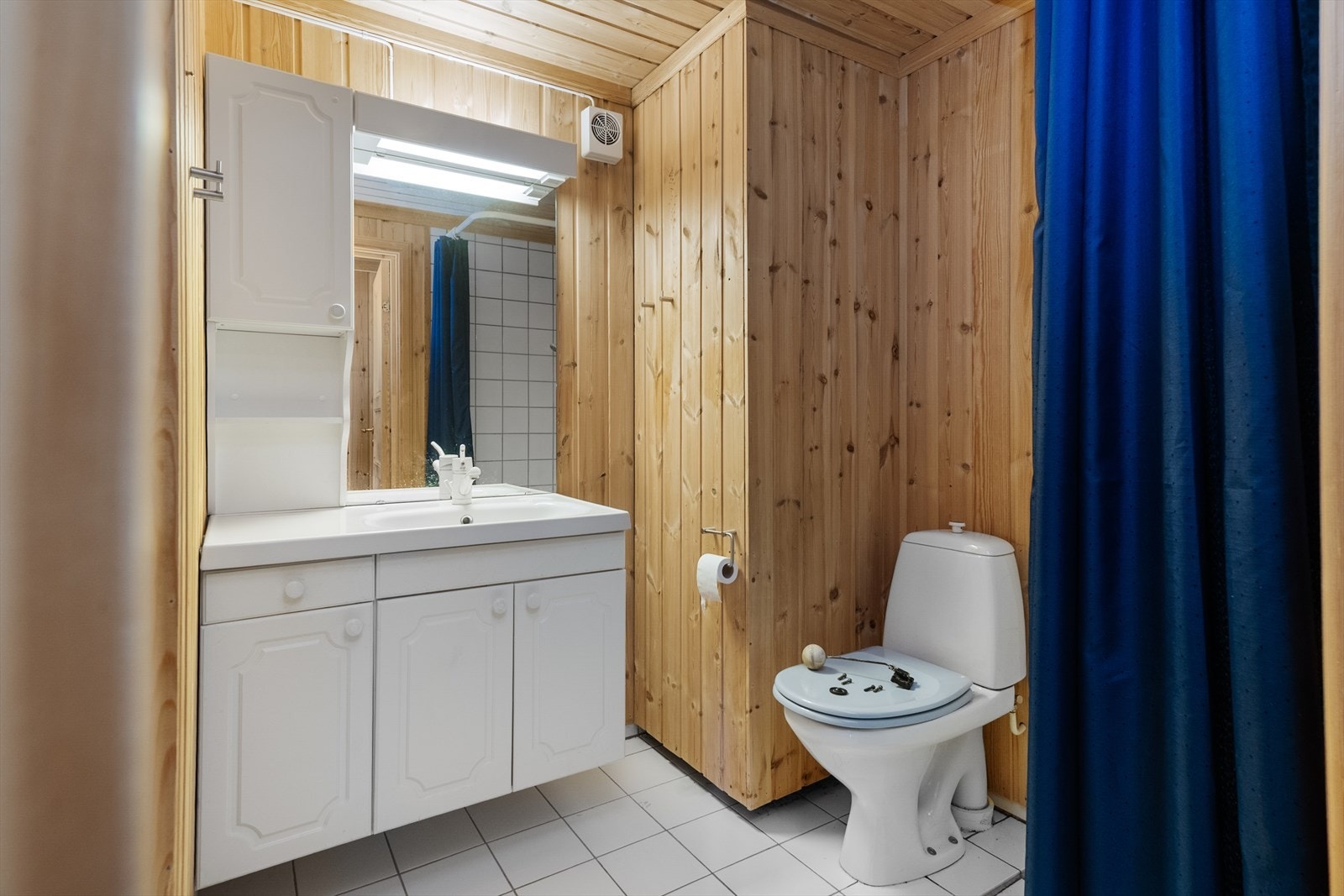 Badet i underetasjen har flis på gulv med varme og inneholder heldekkende servant med underskap, overskap med lys, speil, gulvmontert toalett og dusjhjørne med forheng. Galleribilde