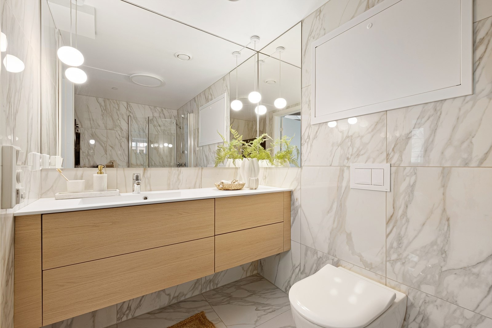 Badet har en stor, trefarget servantinnredning og et speil som dekker store deler av veggen. Nedhengte lamper fra taket gir rommet et elegant og stilfullt uttrykk. Galleribilde