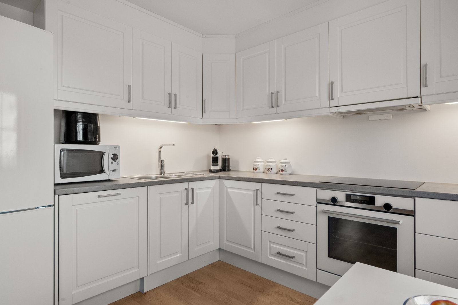 Innredningen har lyse profilerte fronter og laminert benkeplate med nedfelt oppvaskkum. Praktisk med belysning under de takhøye overskapene. Galleribilde