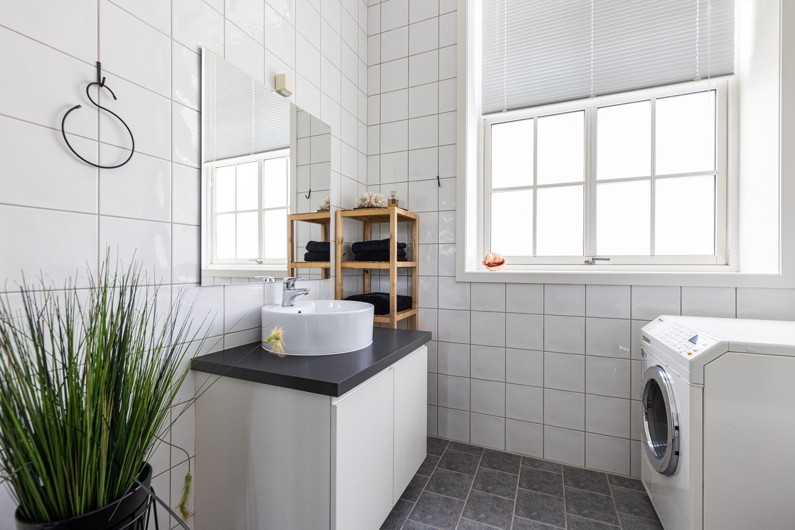 Badet er også innredet med dusjhjørne med plassbesparende, innfellbare glassvegger, veggmontert toalett og opplegg for vaskemaskin. Galleribilde