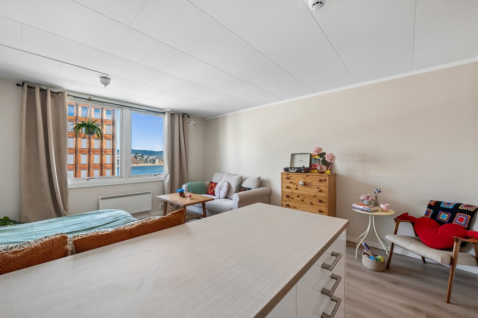 Stilren 1-roms med smart planløsning. Soveplass, stue og åpen kjøkkenløsning i ett, med lysinnslipp fra store vinduer som gir en luftig atmosfære. Galleribilde