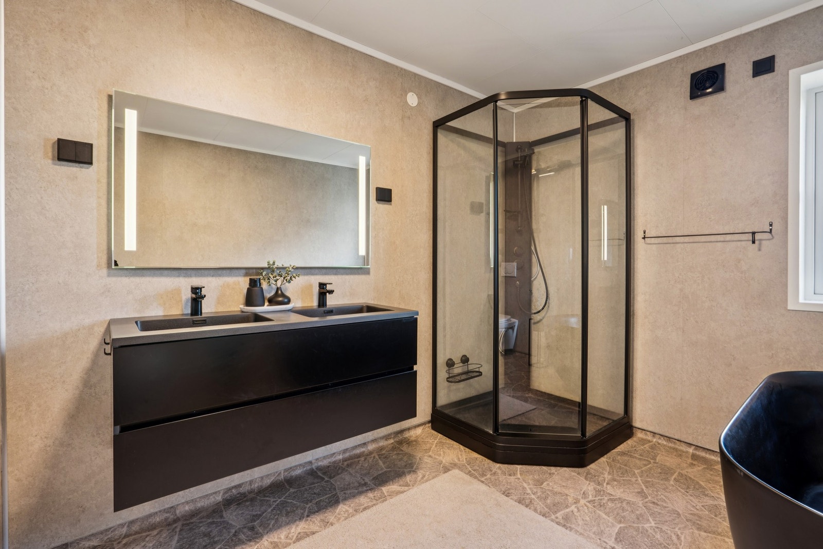 Badet er utstyrt med både et sort dusjkabinett og et frittstående sort badekar for ekstra velvære. Galleribilde