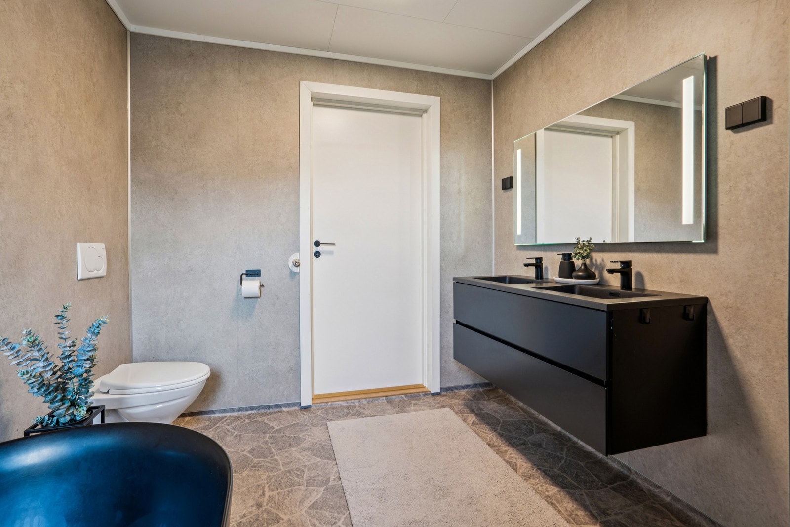 Rommet har vannbåren gulvvarme, vegghengt toalett og en dobbel servant med sorte armaturer. Galleribilde