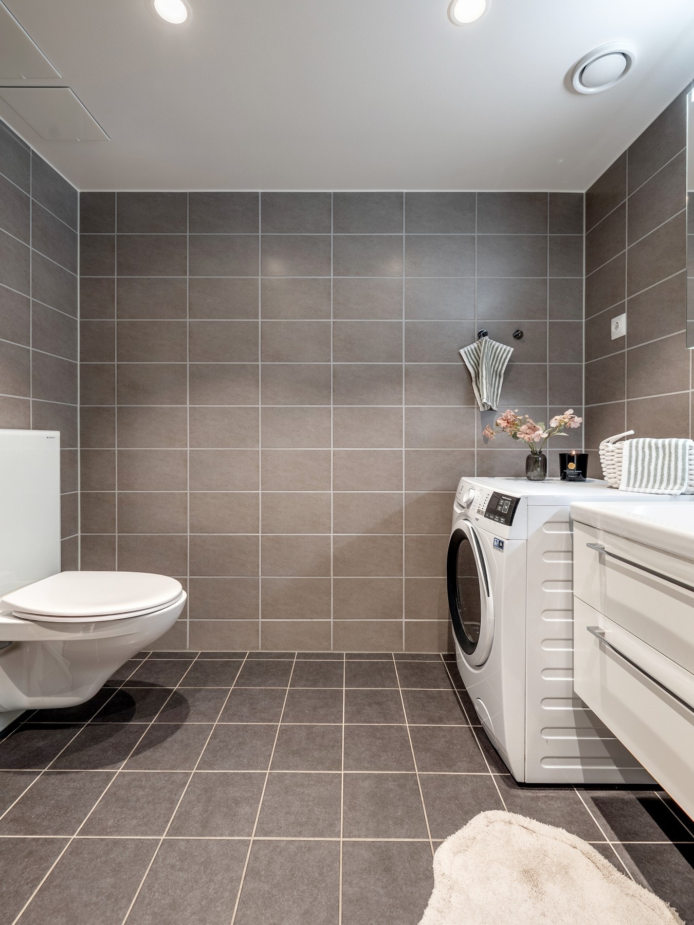 Badet er praktisk plassert i tilknytning til entréen og er pent innredet med fliser på vegger og gulv, varmekabler og innfelt downlights. Galleribilde