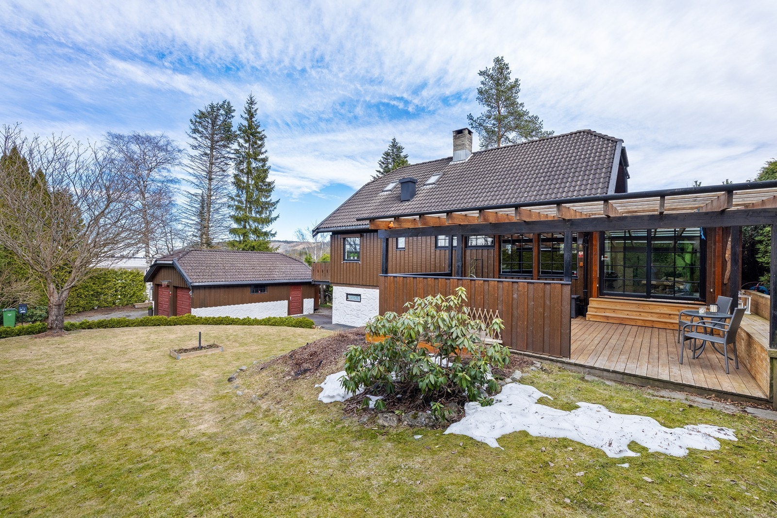 Pent opparbeidet hage med plen og beplantning som gir en grønn og skjermet ramme rundt boligen. Galleribilde