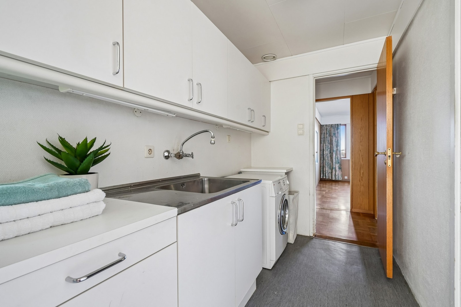 Praktisk vaskerom med våtromsbelegg på gulvet. Innredet med nyere laminat innredning med hvite glatte fronter, stålskyllekum og opplegg for vaskemaskin. Galleribilde