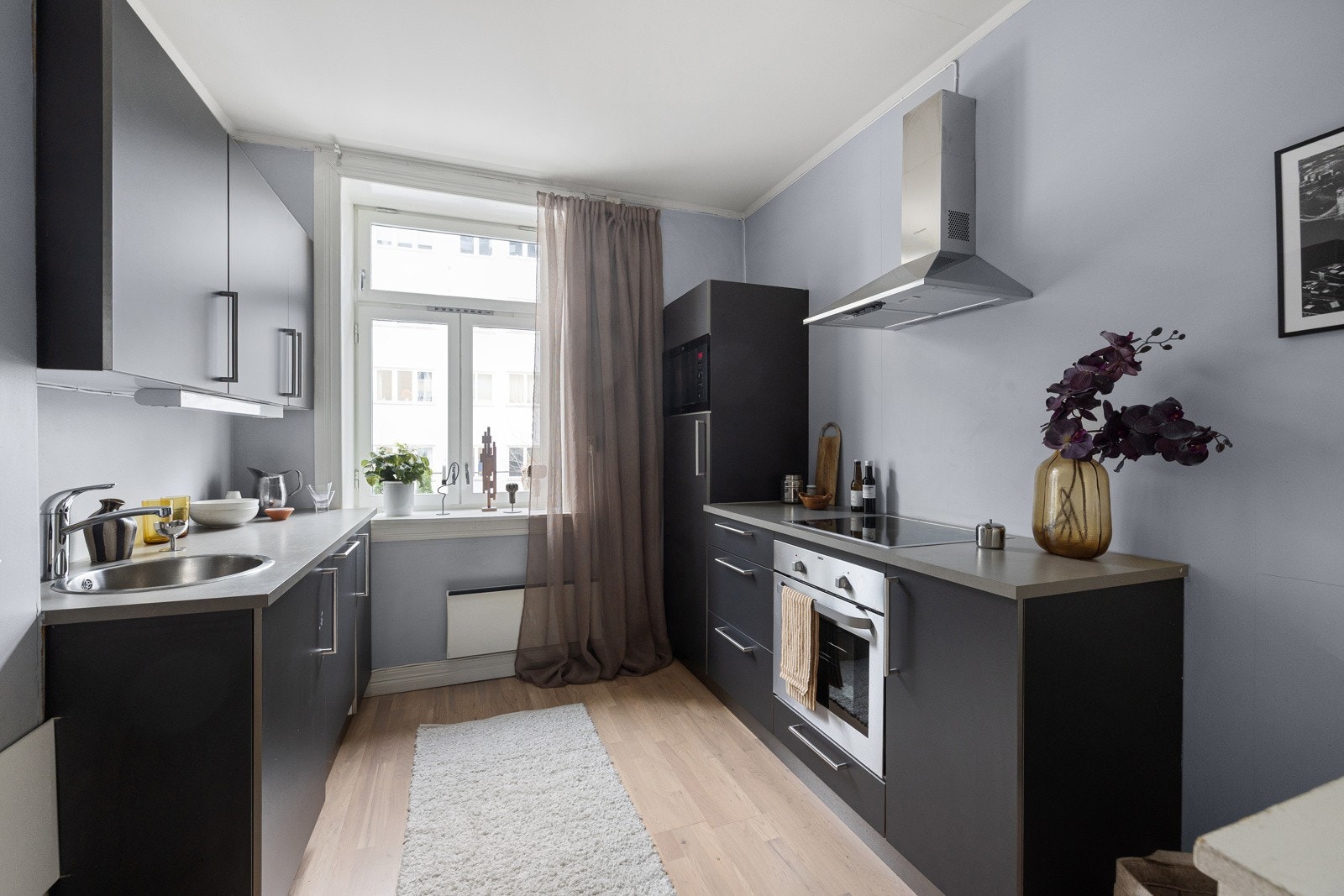 Kjøkkeninnredning med slette og mørklaminert fronter, 28mm tykk og grålaminert benkeplate av spon med nedfelt rund vaskekum i børstet stål og ettgreps blandebatteri i rustfritt stål fra Hans Grohe. Galleribilde