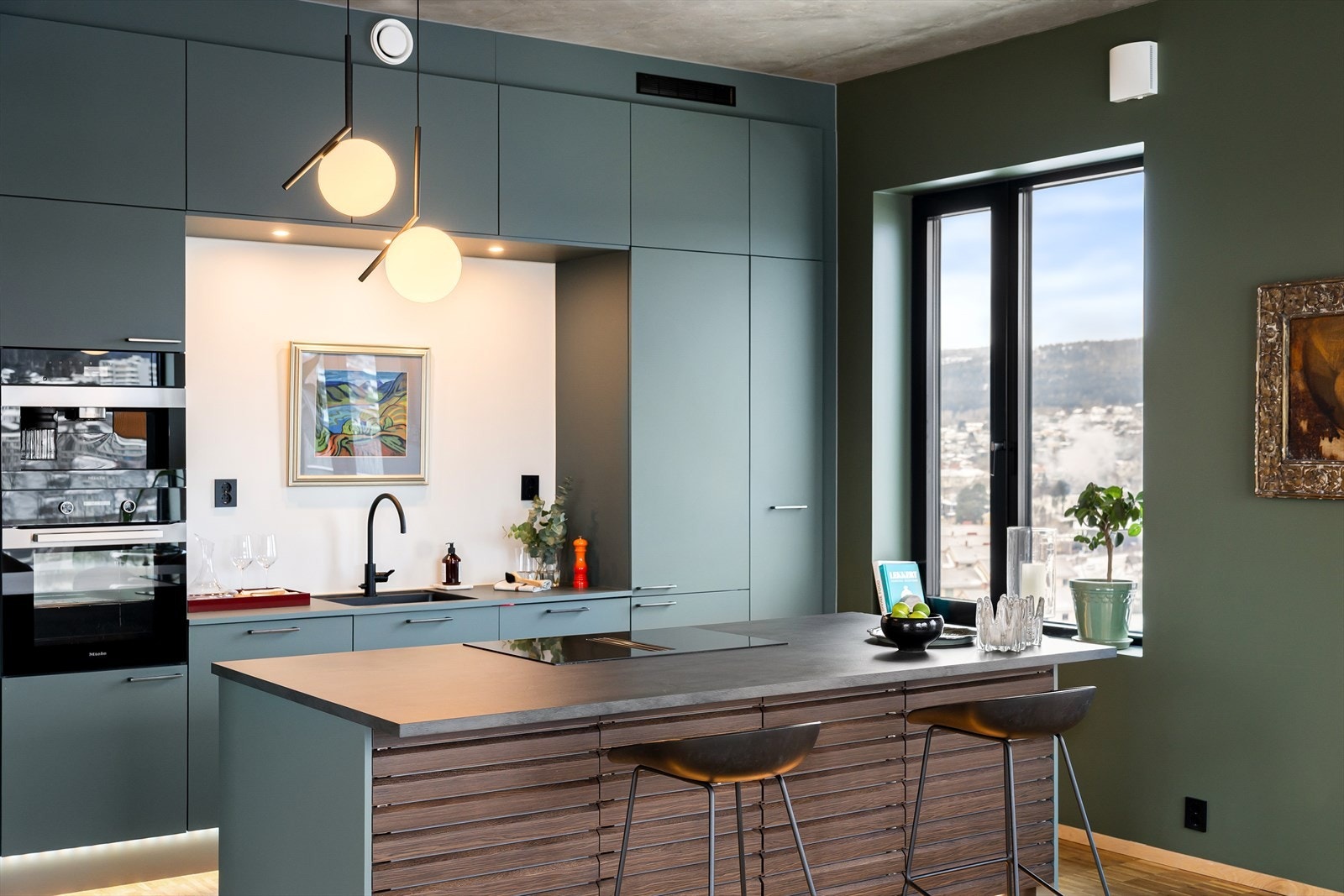 Stilrent og moderne HTH-kjøkken med gjennomført design og dempet grønn/blågrønn fargetone på innredningen, som gir rommet et rolig og særpreget uttrykk. Galleribilde