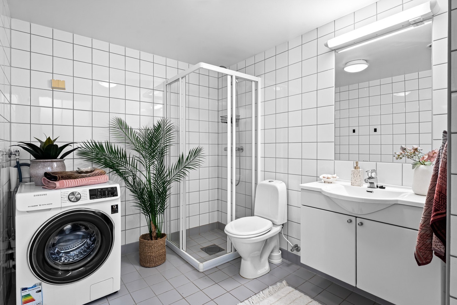 Flislagt baderom med rosmlig dusj, servantseksjon, toalett samt opplegg for vaskemaskin Galleribilde