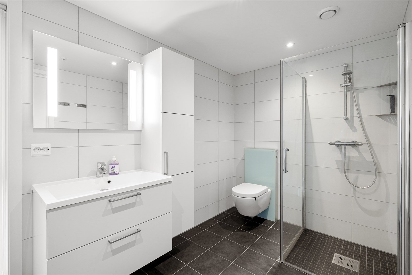 Lekkert helfliset bad med varme i gulv. Badet er utstyrt med servant, vegghengt toalett, dusjhjørne og god lagringsplass i baderomsinnredningen. Spotter i tak for ekstra belysning. Galleribilde