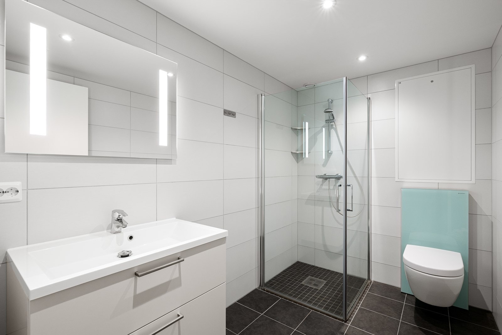 Lekkert flislagt bad med varme i gulv. Badet er utstyrt med servant, dusjhjørne og vegghengttoalett. Spotter i tak for ekstra belysning. Galleribilde