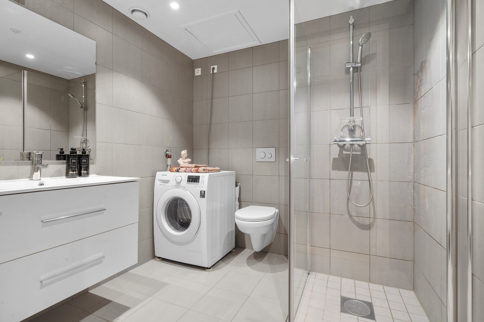 Badet er moderne og pent med veggmontert toalett, dusjhjørne med innfellbare glassdører og opplegg for vaskemaskin. Galleribilde