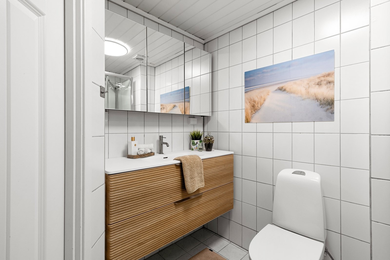 Badet er helfliset, med varmekabler i gulv, og er praktisk plassert mellom soverommene. Det er innredet med toalett, dusjkabinett og servant. Galleribilde