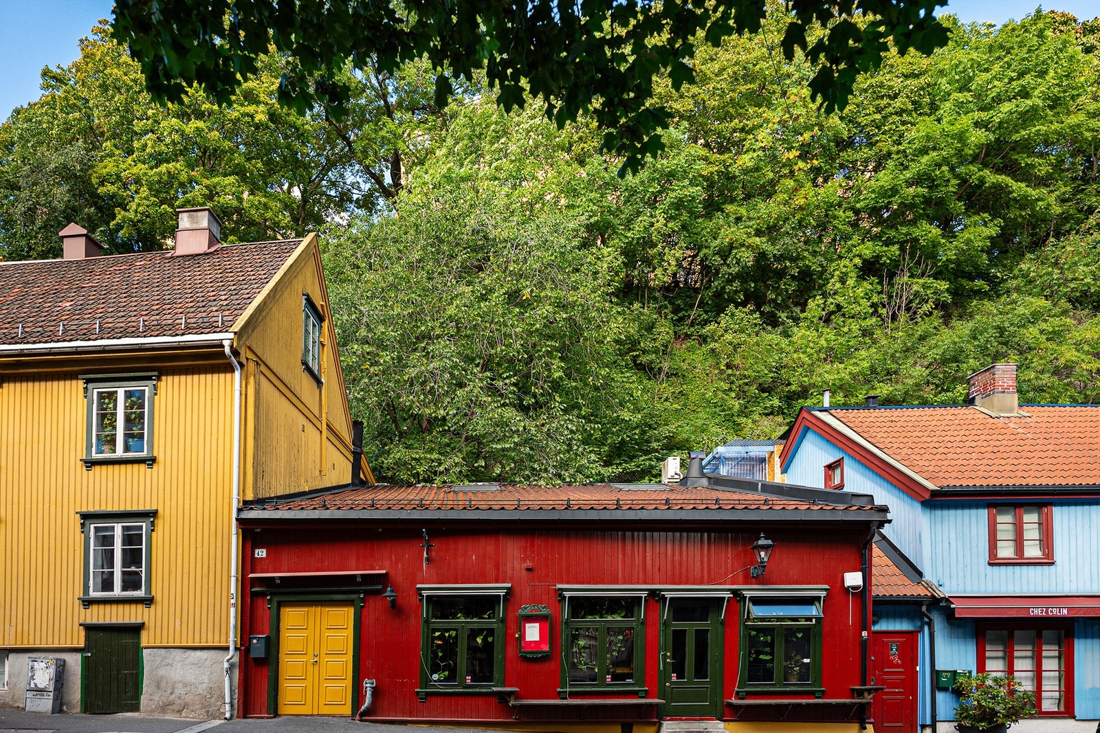 Sjarmerende gatebilde med fargerik trehusbebyggelse, hvor populære Chez Colin i det blå bygget danner et hyggelig og levende miljø sammen med øvrige historiske bygninger i området. Galleribilde