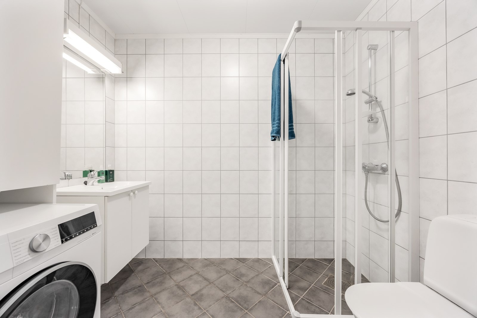 Badet er helfliset og utstyrt med dusjhjørne med skyvedører, servant med speil og lys og et toalett. Galleribilde