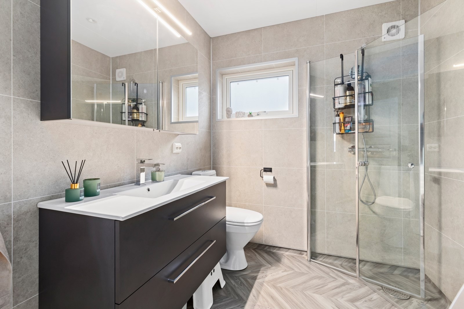 Bad/vaskerom i hovedetasjen ble renovert i 2025 | badet har vinylbelegg med oppkant på gulv og våtromsplater på vegger | rommet er utstyrt med baderomsinnredning, vegghengt dusj med dusjvegger, wc og opplegg for vaskemaskin og tørketrommel Galleribilde