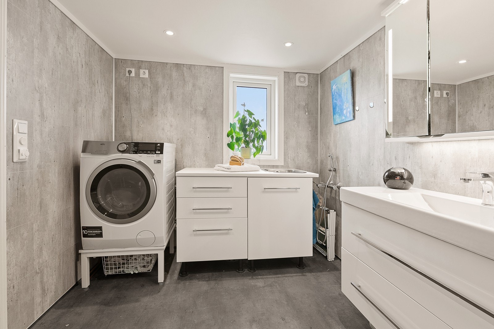 Badet inneholder vegghengt wc, dusjhjørne, håndvask med skuffer og speilskap. Vaskekum med tilpassede skap og opplegg for vaskemaskin. Galleribilde