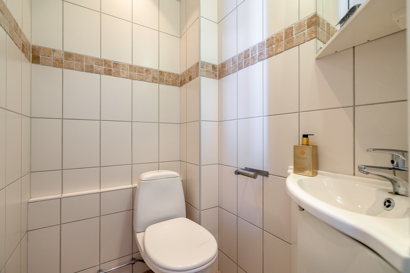 Toalettrommet er praktisk og funksjonelt med flislagte vegger og gulv. Rommet er innredet med toalett og servant med speil over. Galleribilde