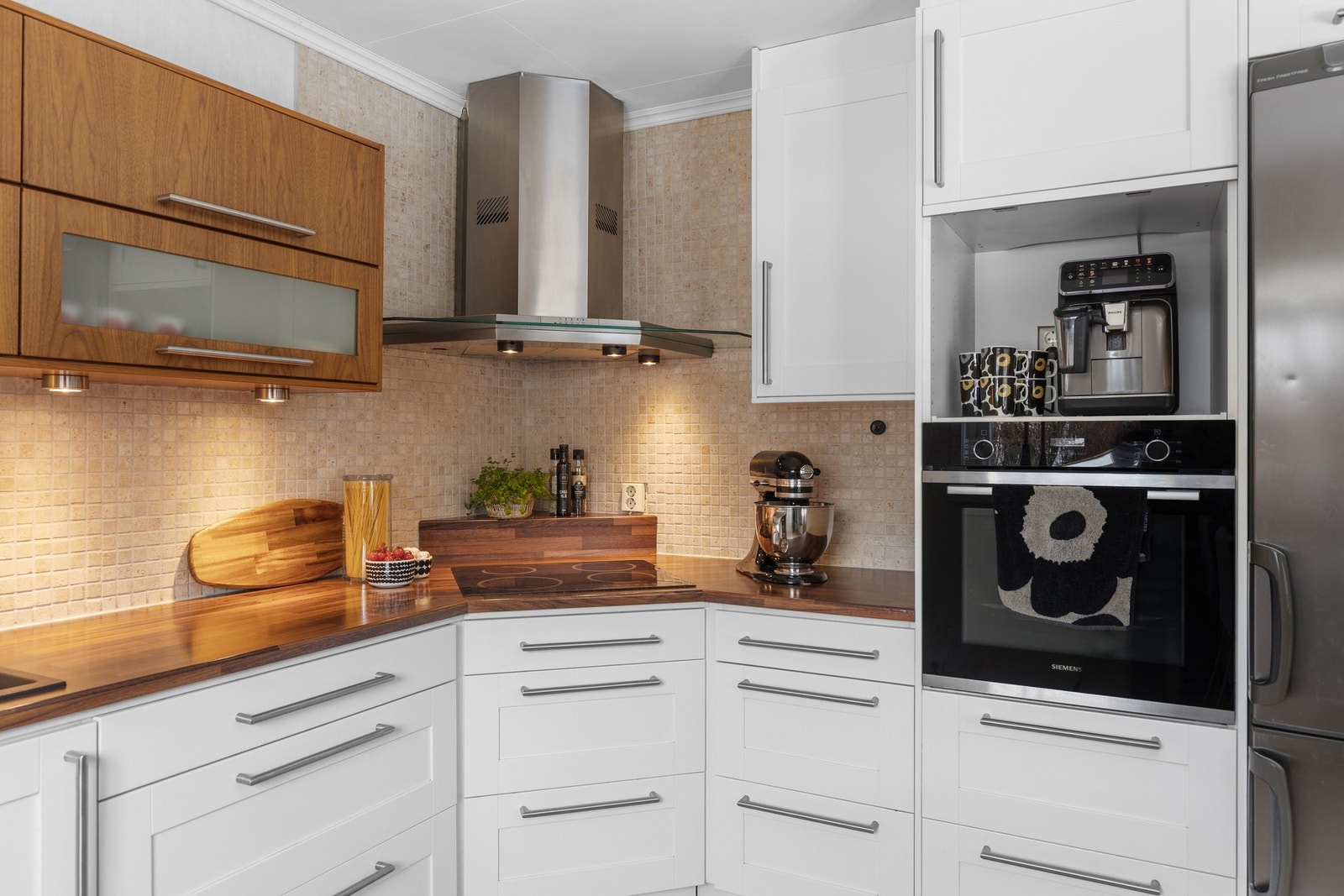 Integrerte hvitevarer består av oppvaskmaskin, platetopp og stekeovn i praktisk høyde. Dekorative fliser og god belysning over benken. Galleribilde