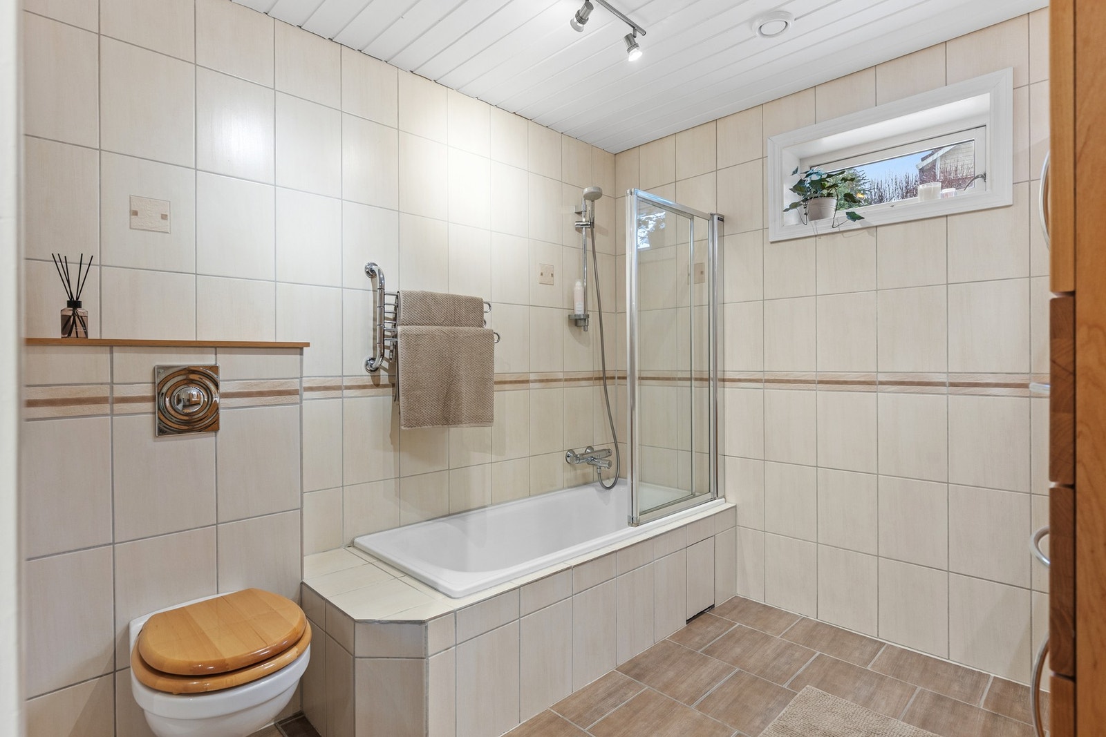 Romslig, flislagt baderom med varmekabler, badekar med dusjløsning og vegghengt toalett - et praktisk og komfortabelt bad for hele familien. Galleribilde