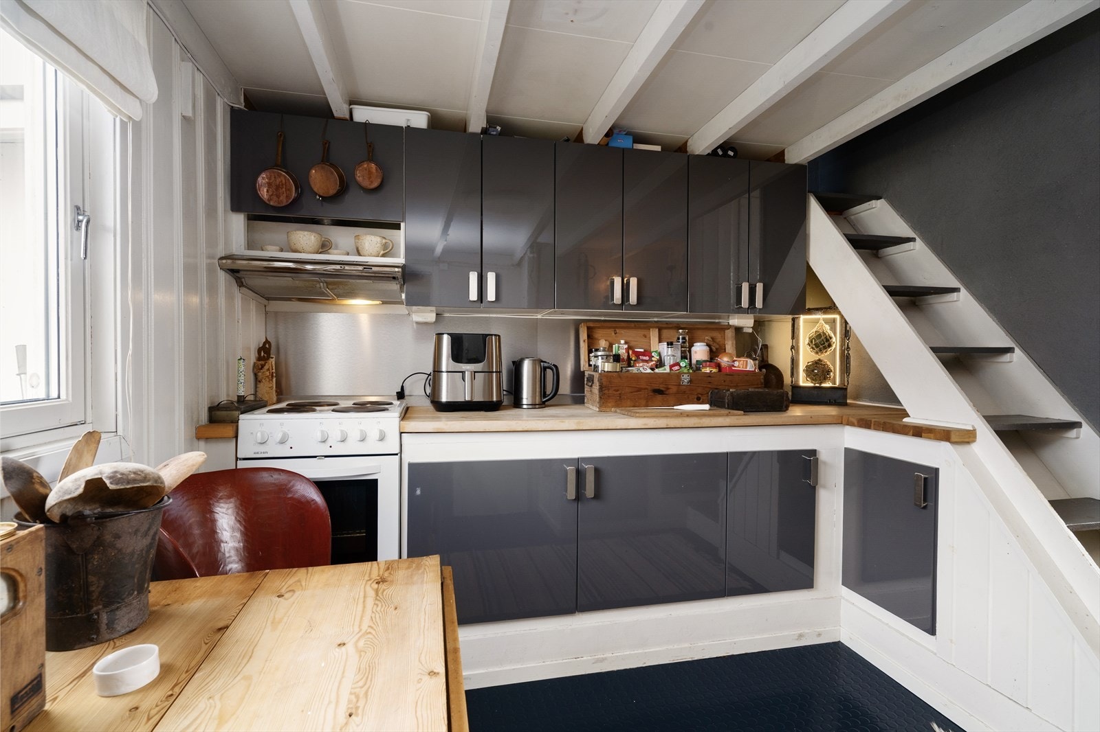 Koselig kjøkken med plass til en mindre spisegruppe ved vindu. Kjøkkeninnredningen består av eldre, plassbygde underskap og nyere overskap med fronter i høyglans. Galleribilde