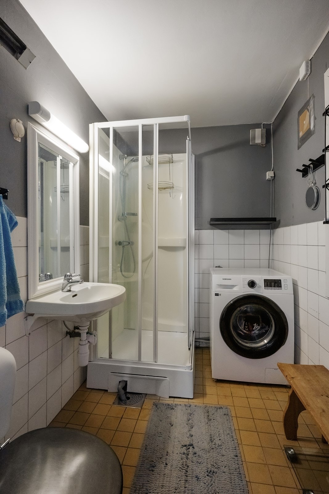 Kombinert bad- og vaskerom av eldre dato. Her er det gulvmontert toalett, veggmontert servant og dusjkabinett, samt opplegg for vaskemaskin. Oppvarming via stråleovn. Galleribilde