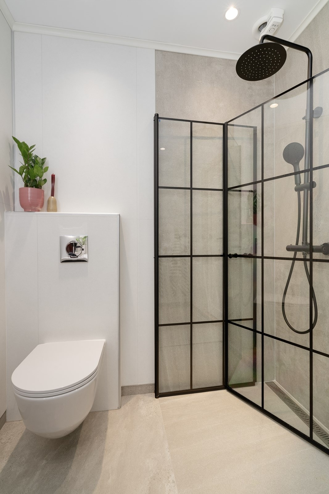 Flislagt dusjhjørne med innfellbare dusjvegger og praktisk dusjsett med blandebatteri, tak- og hånddusj. Lyse våtromsplater i flisimitasjon på vegger og malt tak med innfelte spotter. Galleribilde